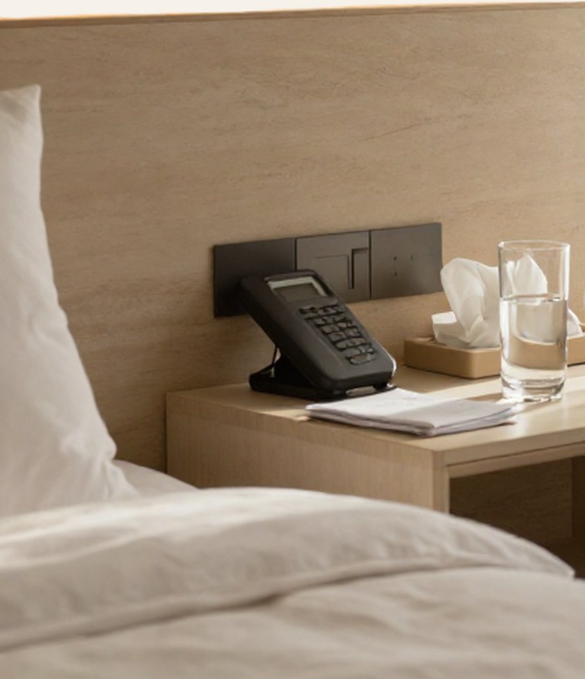 Bedside table with a phone, tissues, a glass of water, and written instructions next to the bed
